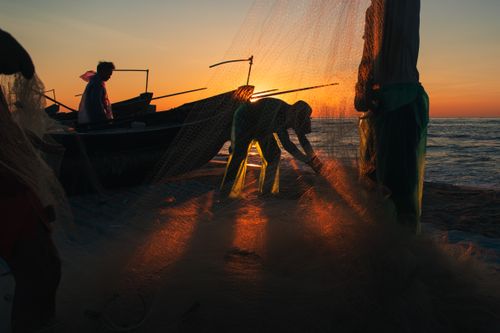 Free Fishermen managing nets at sunset on a Vietnamese beach, capturing a serene silhouette scene. Stock Photo
