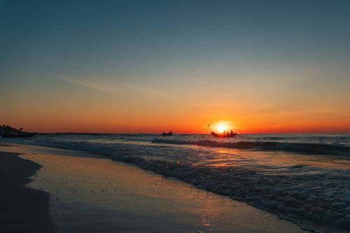 Free Captivating sunset at Quảng Trị beach, Vietnam, featuring a silhouetted boat on calm waves. Stock Photo
