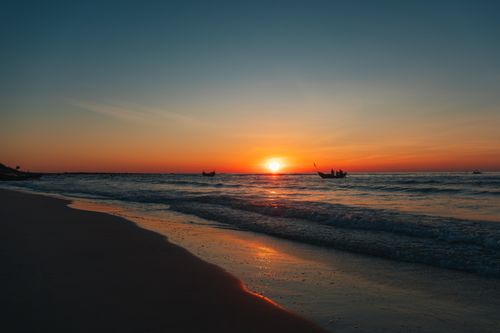 Free Serene beach sunset in Quảng Trị, Vietnam with boats silhouetted against the vibrant horizon. Stock Photo