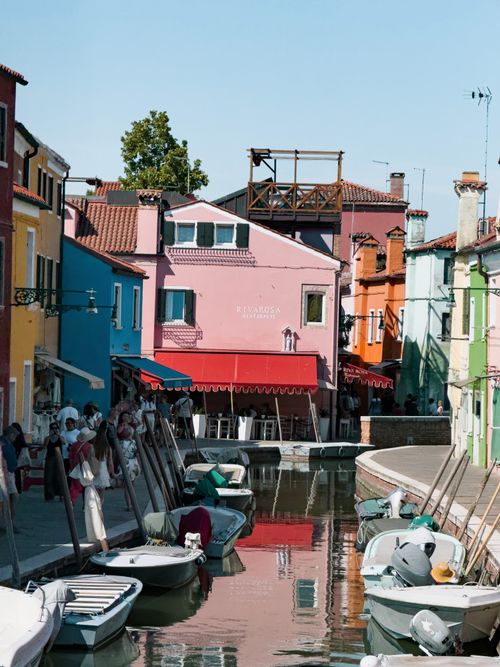 Free Vibrant colored houses and boats line a sunny canal in Burano, Italy, capturing its charming allure. Stock Photo