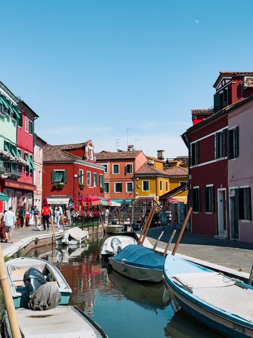 Free Vibrant canal with boats and colorful houses in Burano, Italy under a clear sky. Stock Photo