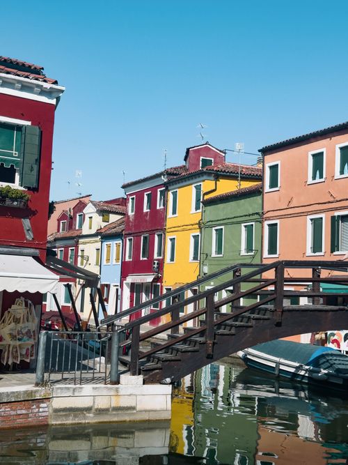 Free Vibrant colored houses line a canal in Burano, Italy, under a clear blue sky. Stock Photo