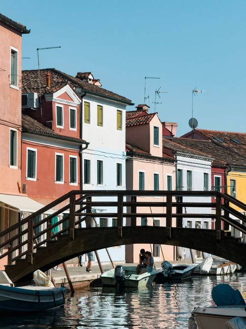 Free Vibrant houses along Burano canals with a quaint wooden bridge under a clear summer sky. Stock Photo