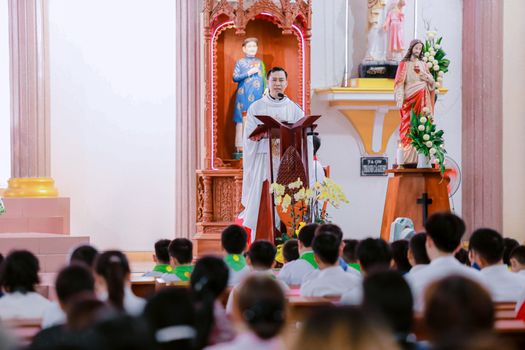 A priest delivering a sermon to a congregation inside a church with religious statues in the background.