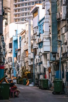 A narrow urban alley lined with buildings featuring numerous air conditioners and garbage bins, creating a dense cityscape.