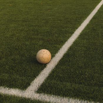 A lone soccer ball rests on a vibrant green field, marked with white lines.