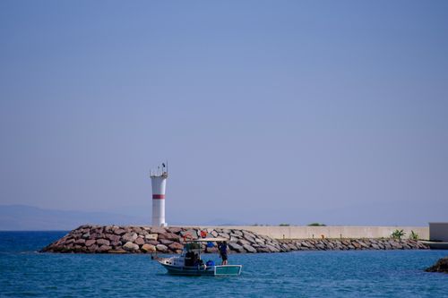 Free Fishing boat near lighthouse on a sunny day in İzmir, Türkiye, showcasing a peaceful coastal view. Stock Photo