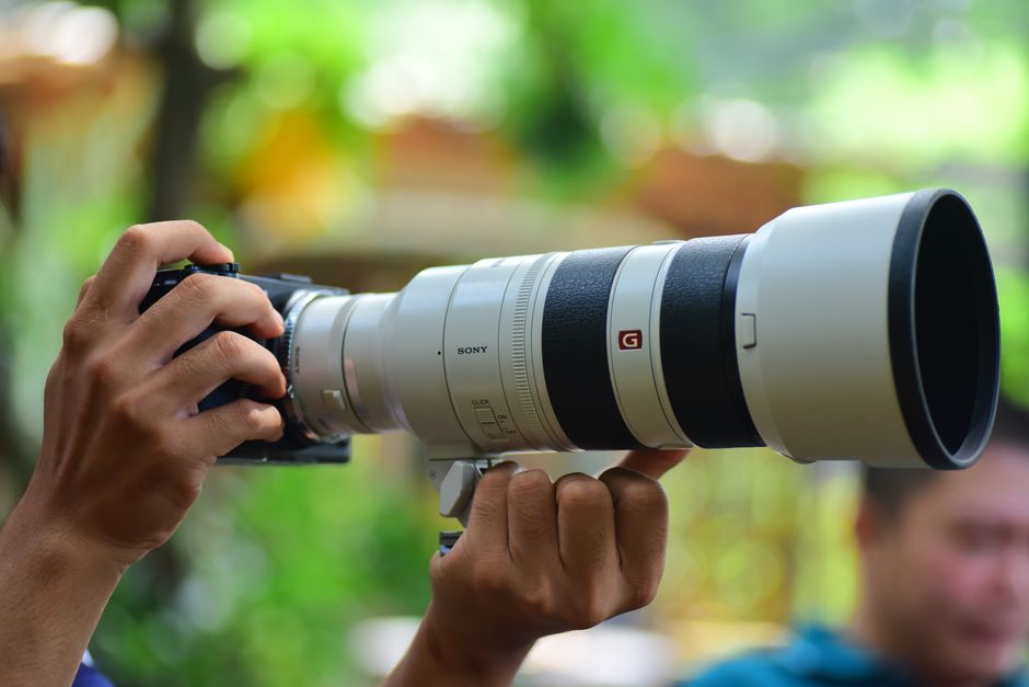 Fotógrafo segurando câmera mirrorless com objetiva teleobjetiva de grande porte em ambiente externo