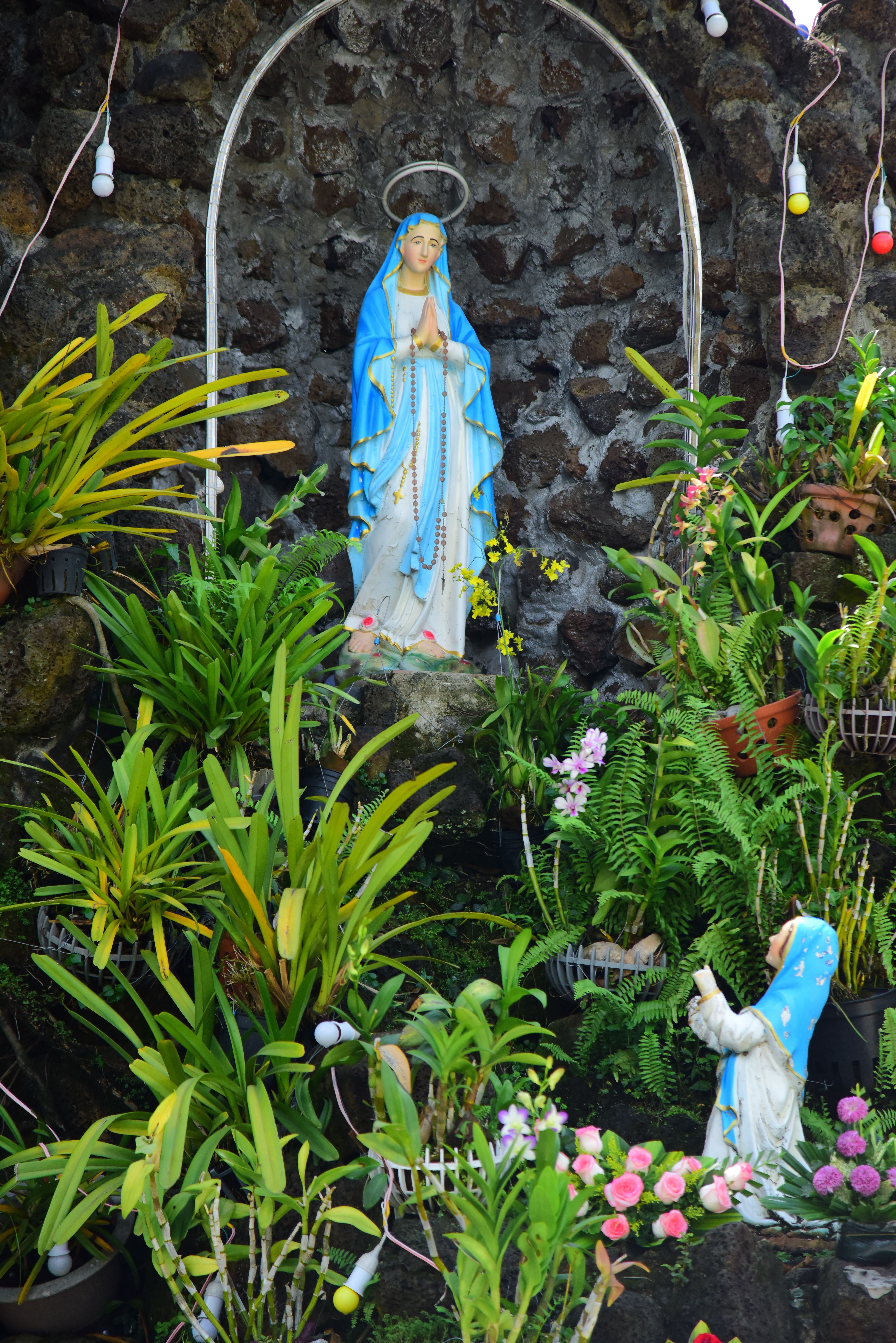 A serene garden shrine featuring a statue of the Virgin Mary surrounded by lush greenery.