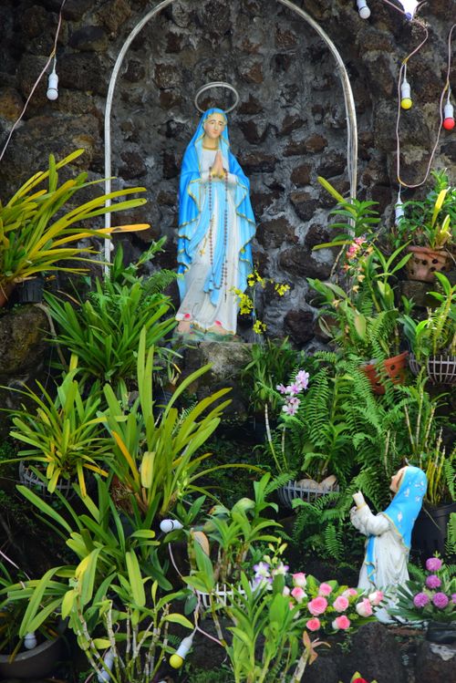 Free A serene garden shrine featuring a statue of the Virgin Mary surrounded by lush greenery. Stock Photo