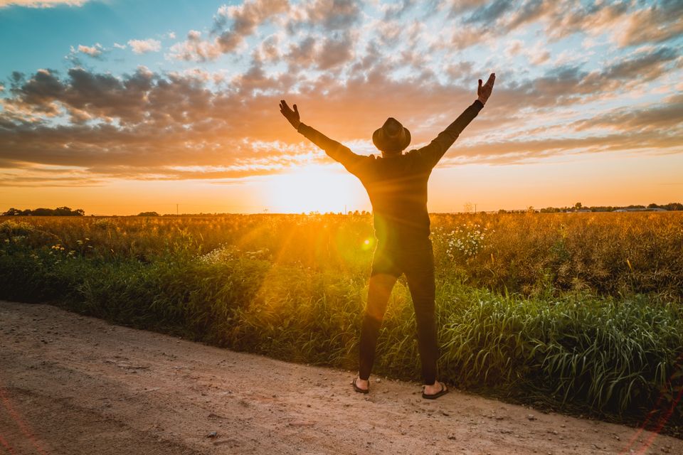 A man raising his arms at sunrise in an open field