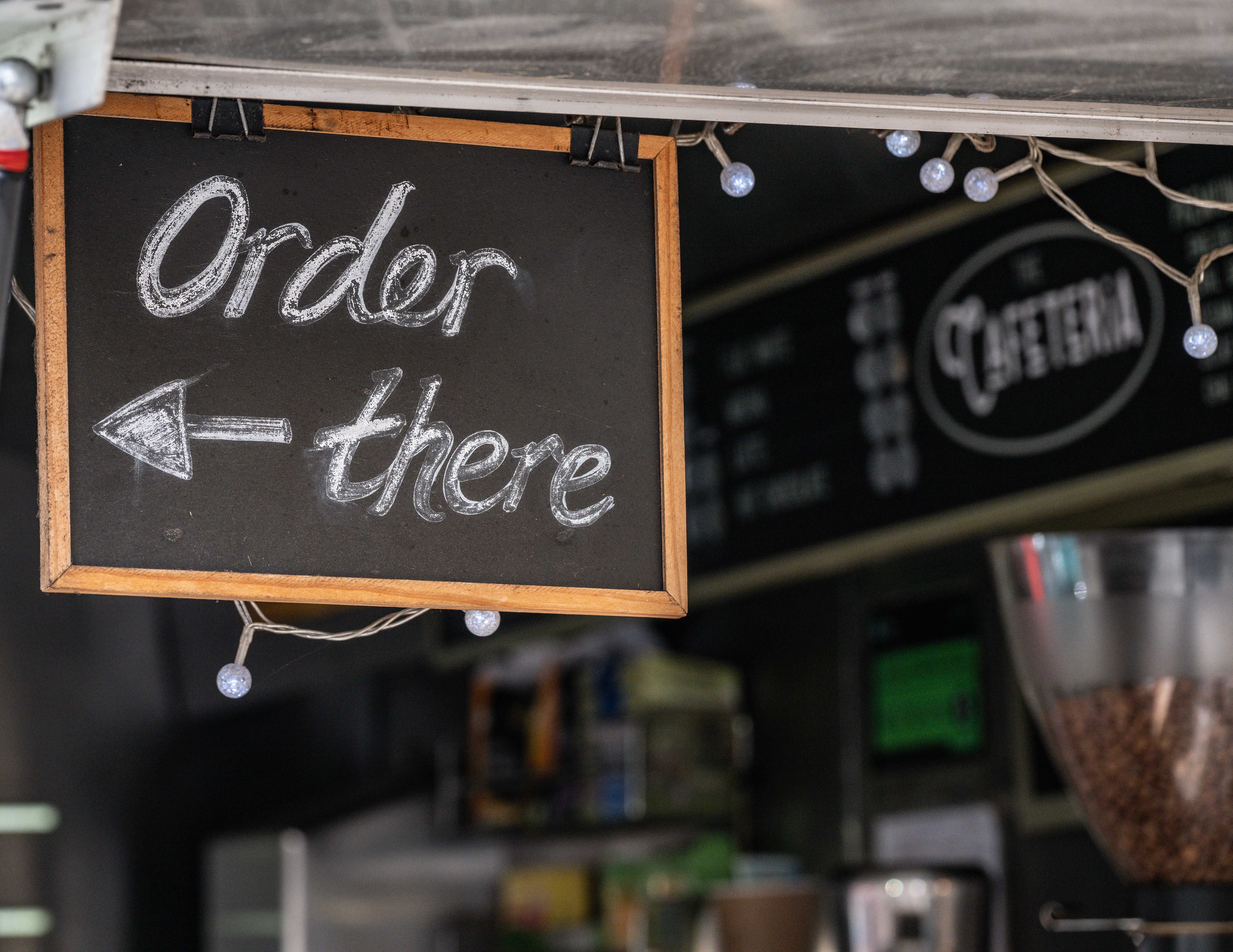 Chalkboard sign directing to order inside a cozy cafe with festive lights.