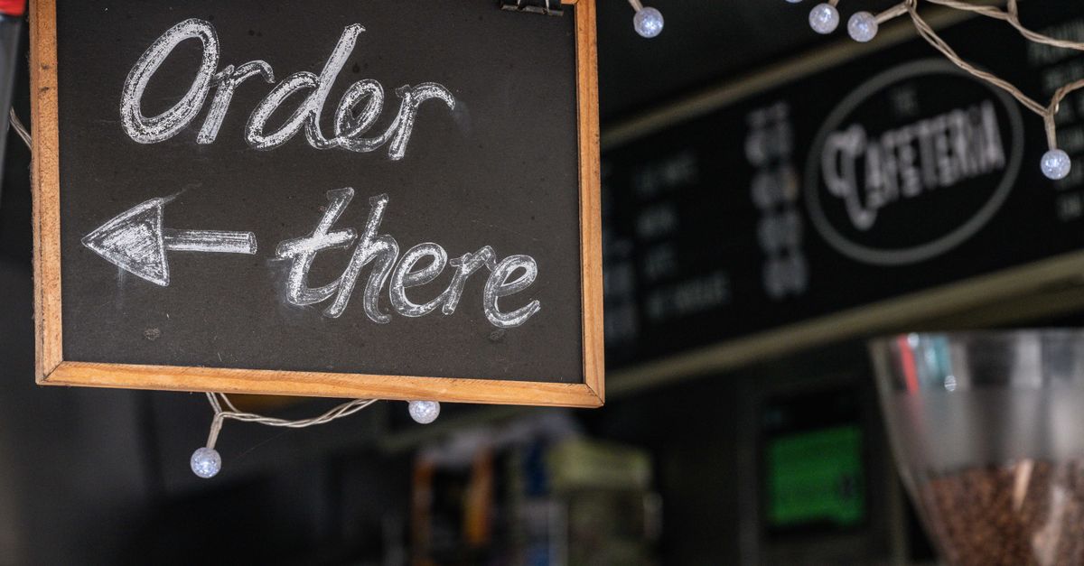 Chalkboard sign directing to order inside a cozy cafe with festive lights.