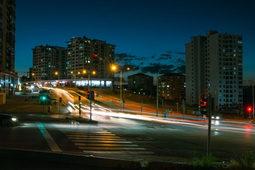 A vibrant city intersection at night with light trails from passing vehicles and illuminated buildings.