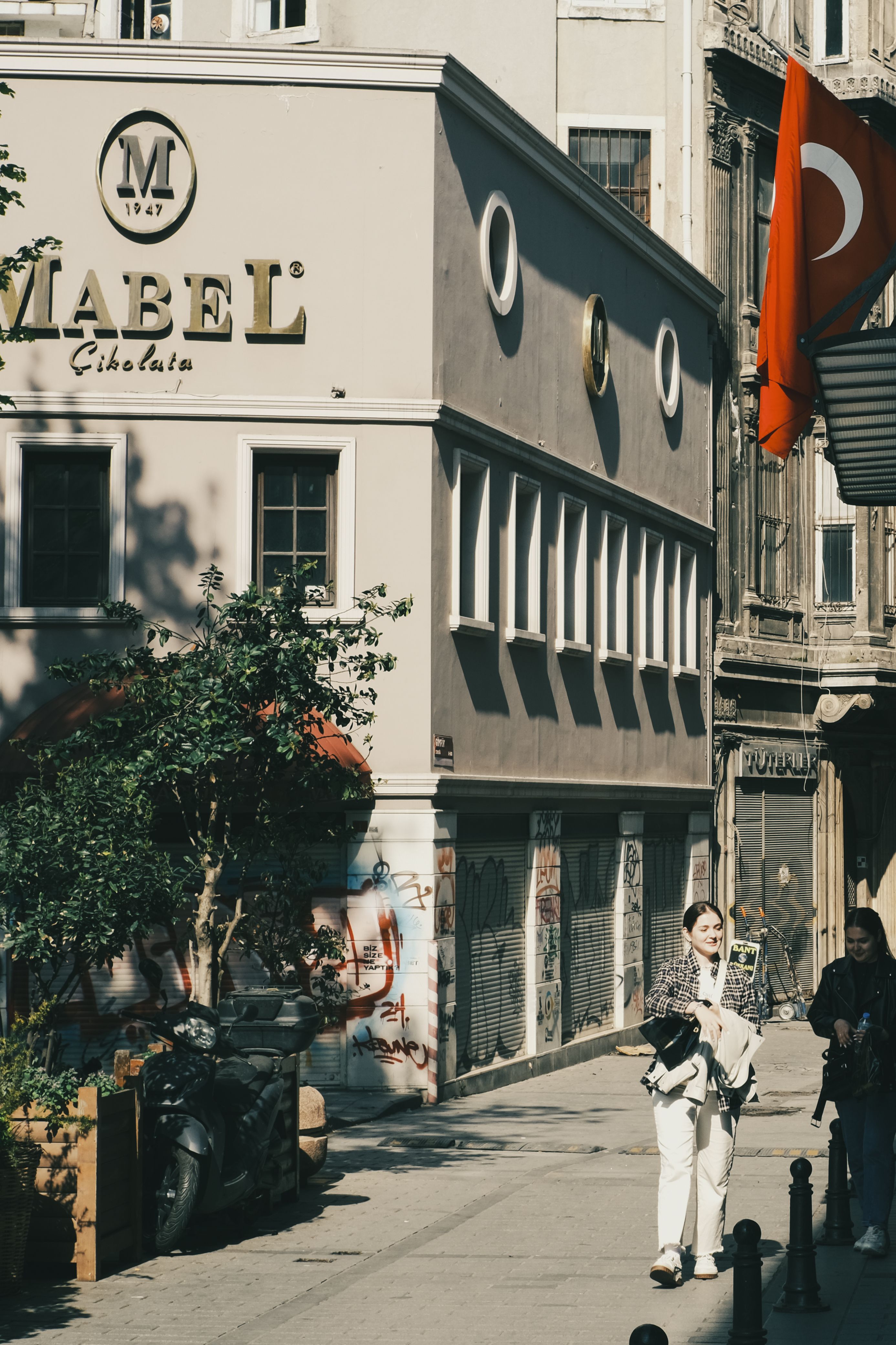 Urban street scene in Istanbul featuring Mabel Chocolate shop facade and Turkish flag.