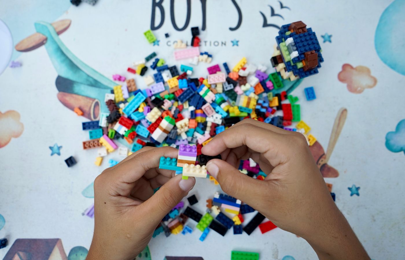 Hands of a child assembling colorful Lego bricks on an outdoor table, showcasing creativity and playfulness.