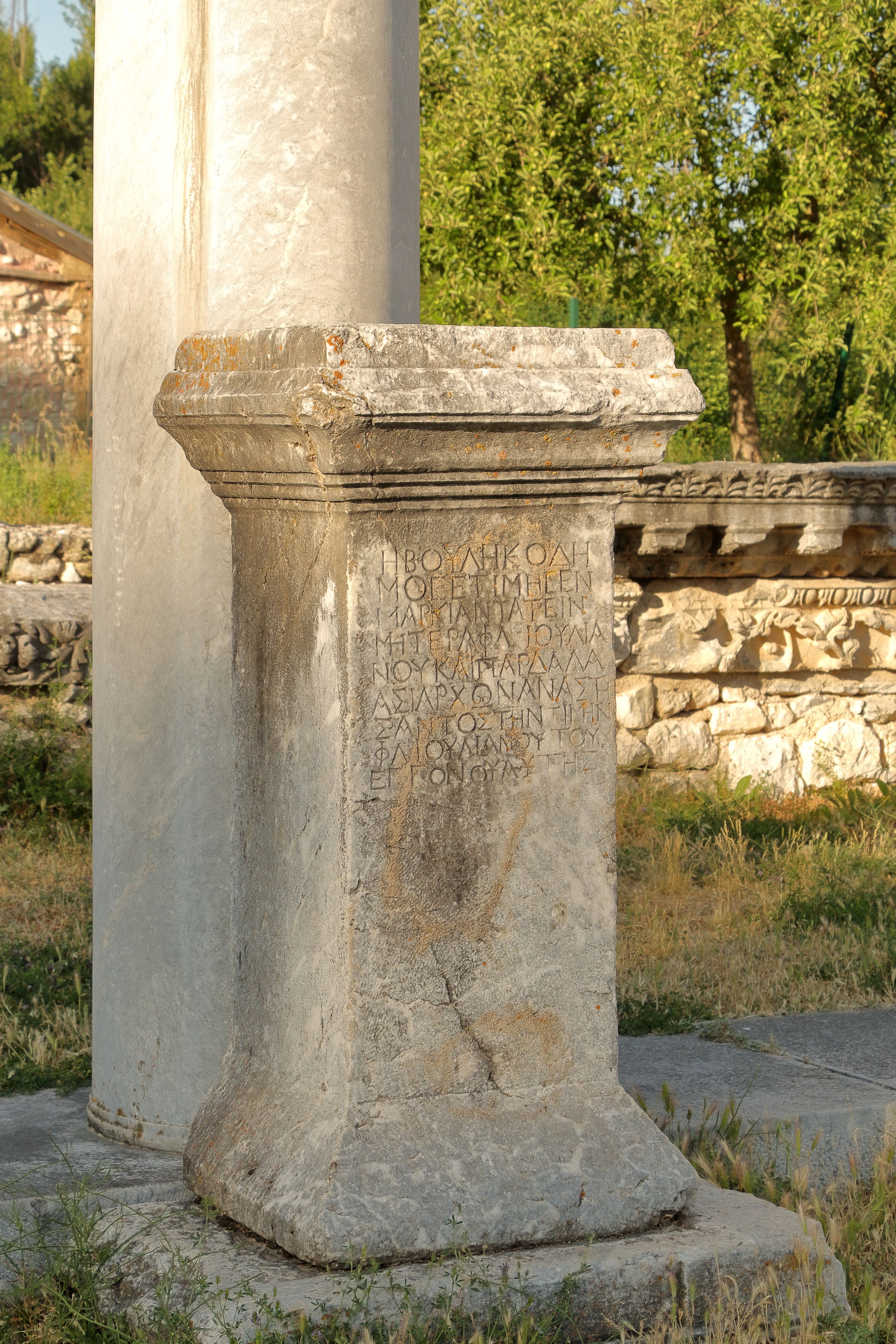 Close-up of a historic stone column featuring Greek inscriptions, located outdoors in an ancient setting.