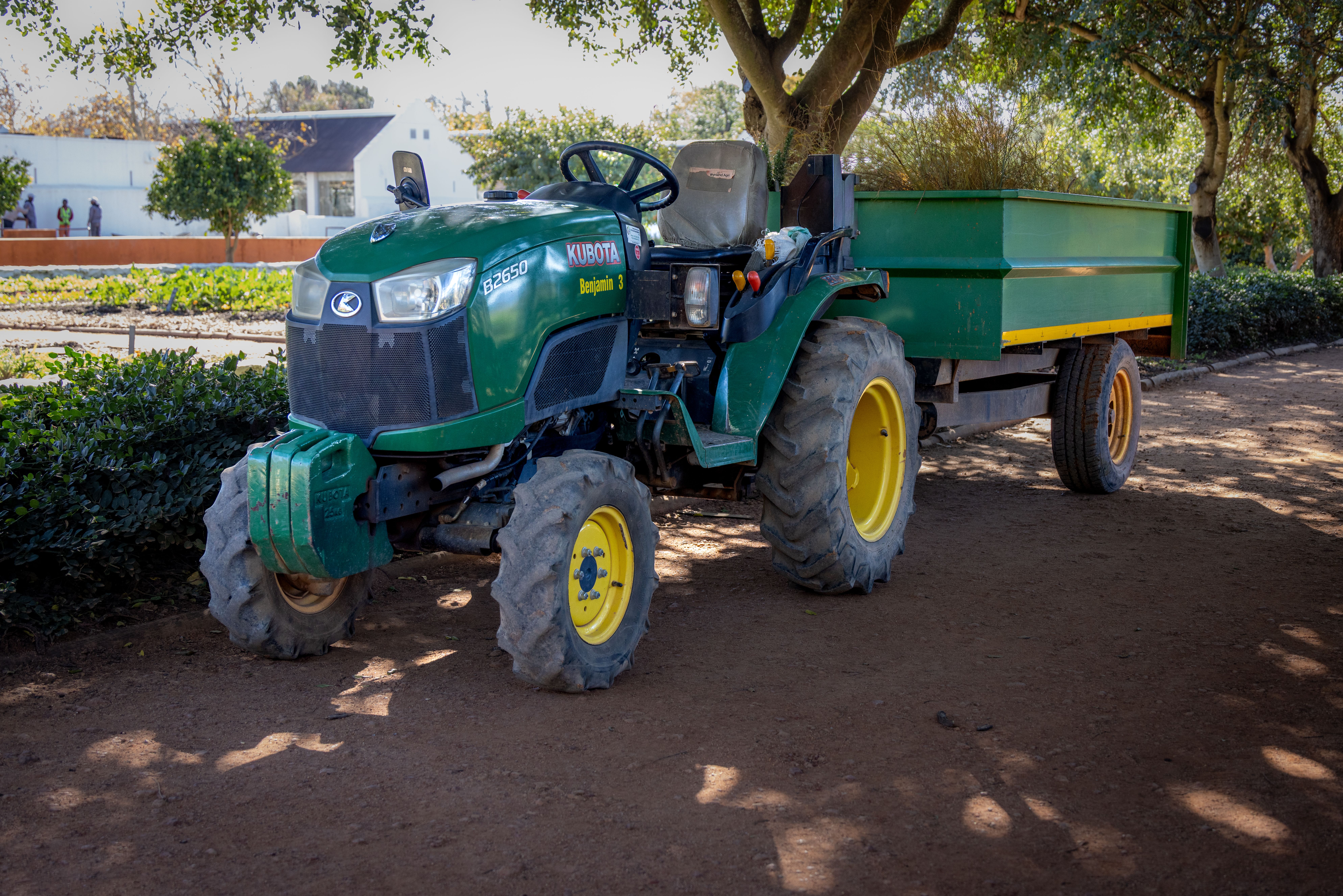 A vibrant green tractor with a trailer parked in a sunny farm setting, ideal for agricultural themes.