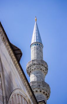 Detailed view of a mosque minaret in Istanbul with intricate architecture set against a clear blue sky.