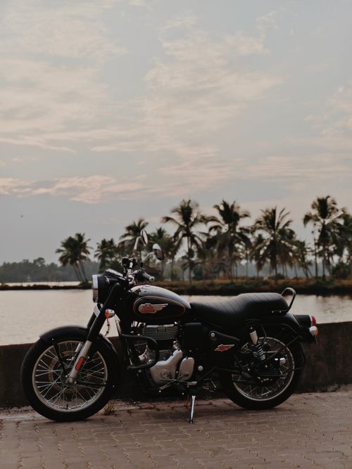 Free Vintage motorcycle parked near a tropical waterfront at sunset with palm trees in the background. Stock Photo