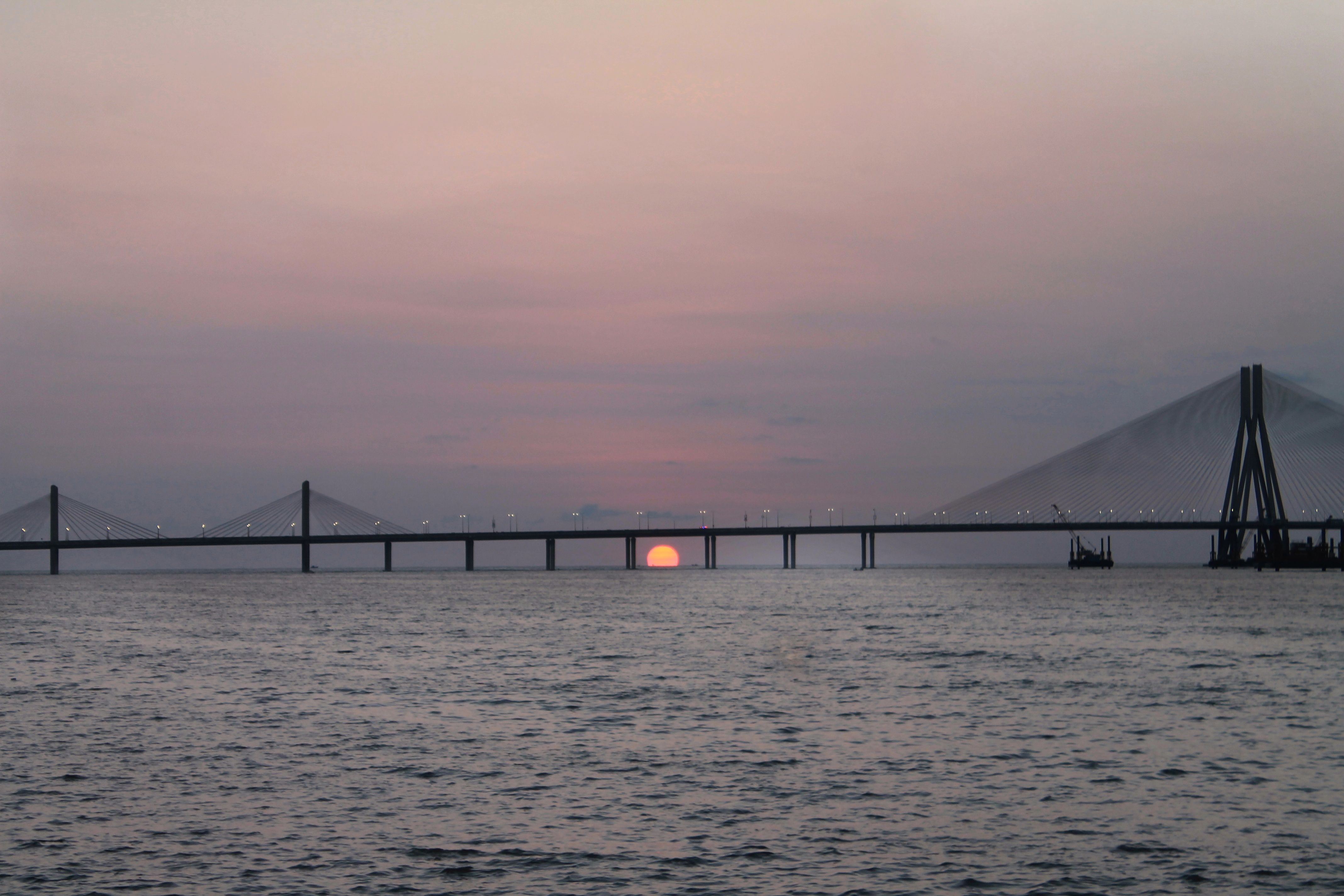 Sun setting behind the Bandra-Worli Sea Link seen from a rocky headland