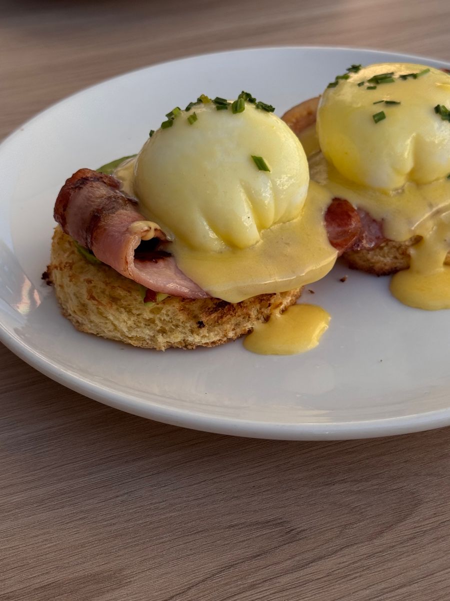 Eggs Benedict with hollandaise and chives on a white plate