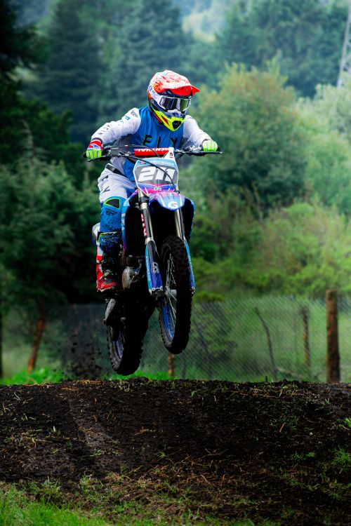 Free Motocross rider performing a thrilling jump on a dirt track in Mexico City, surrounded by lush greenery. Stock Photo