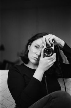 A woman holding a camera takes a portrait in monochrome.