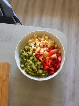 A top view of a vibrant fruit salad in a white bowl with kiwi, apple, and strawberry.