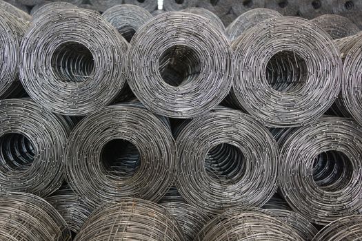 Stacked coiled steel wire mesh rolls captured in a warehouse setting.