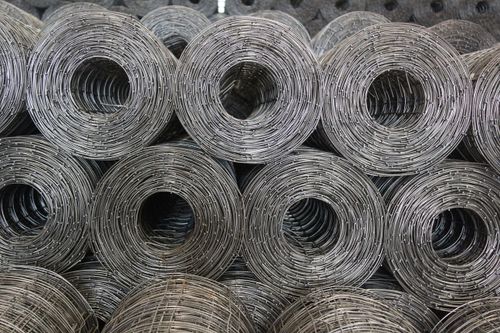 Free Stacked coiled steel wire mesh rolls captured in a warehouse setting. Stock Photo