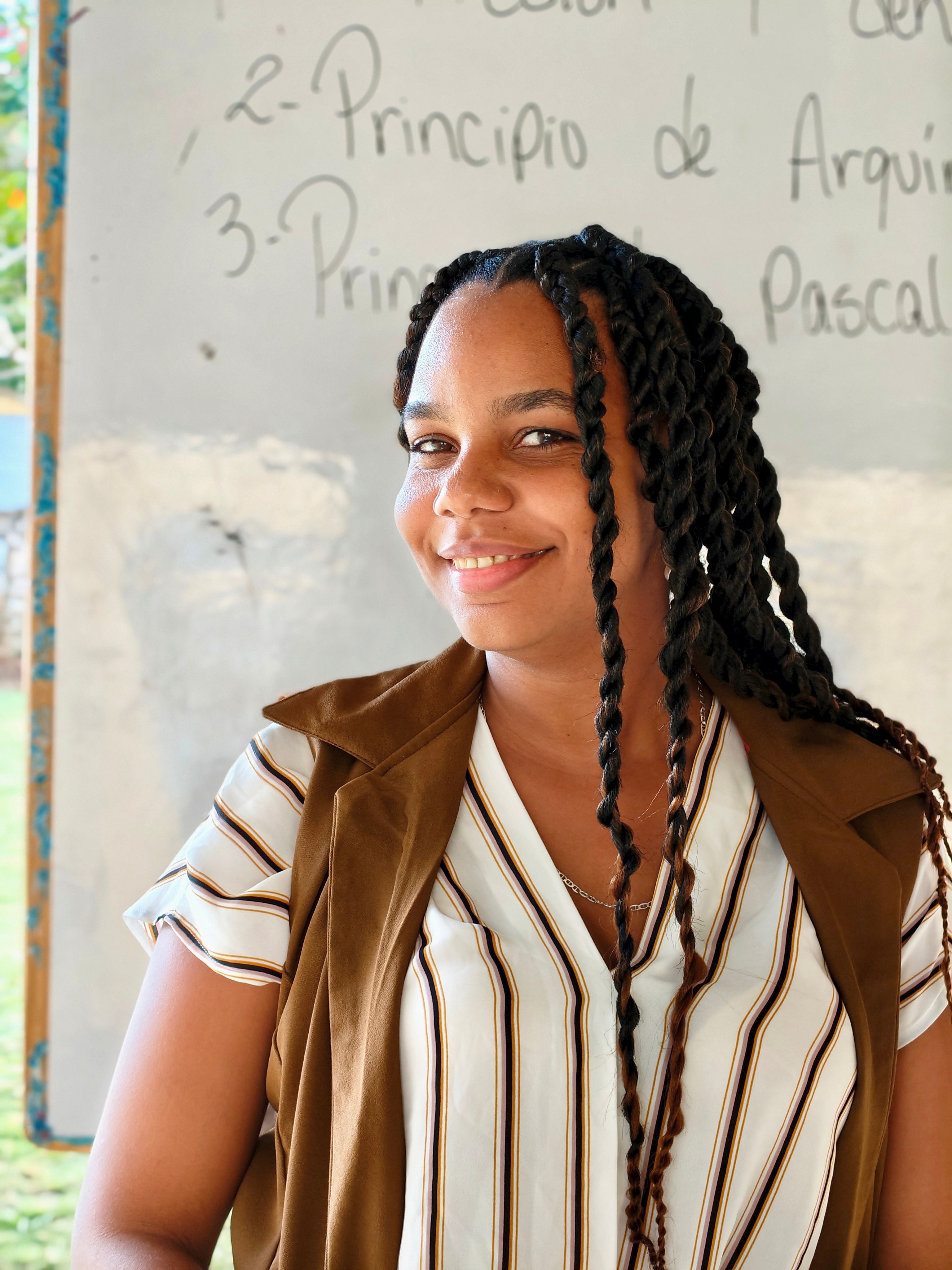 A woman smiles in a classroom with notes on the board behind her.