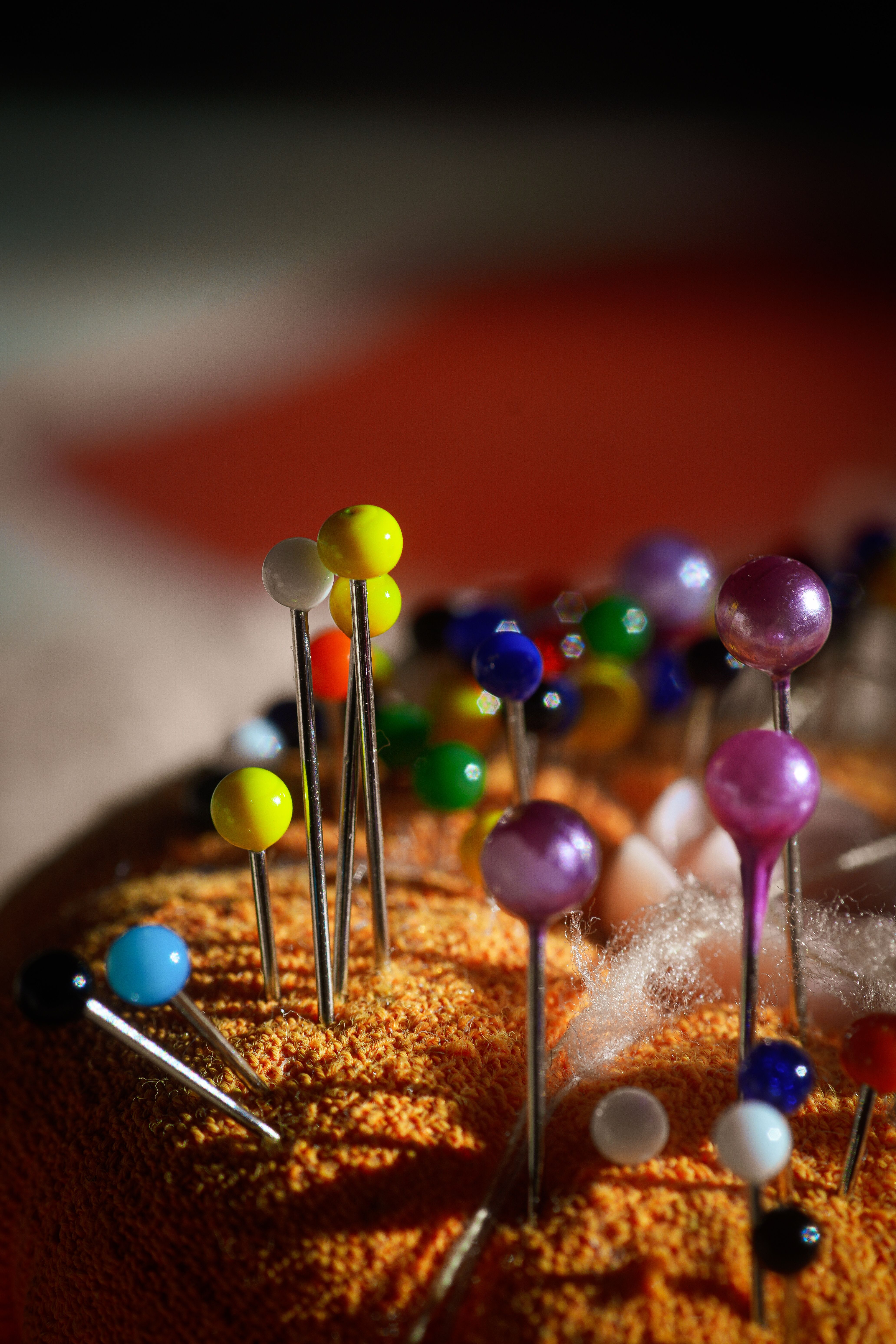 Close-up of colorful sewing pins on a cushion, highlighting creativity in vibrant lighting.