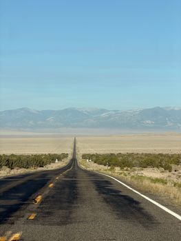 A long, straight highway stretches through a desert landscape towards distant mountains under a clear blue sky.