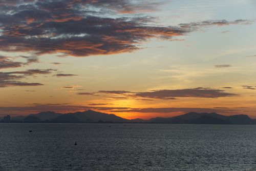 Free A serene view of the sun setting behind mountains over the ocean horizon. Stock Photo
