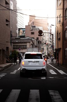 A luxurious white SUV drives through a busy street in central Tokyo, Japan, showcasing urban elegance.
