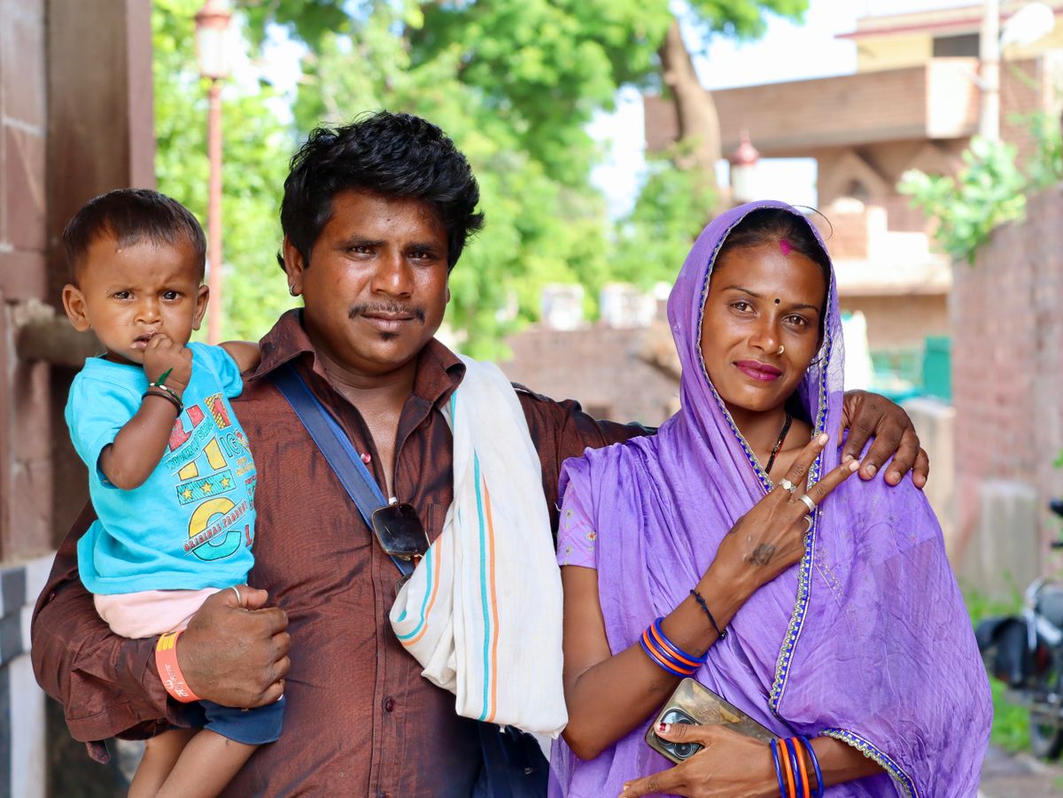 A smiling family standing together, a father holding his young child beside the mother