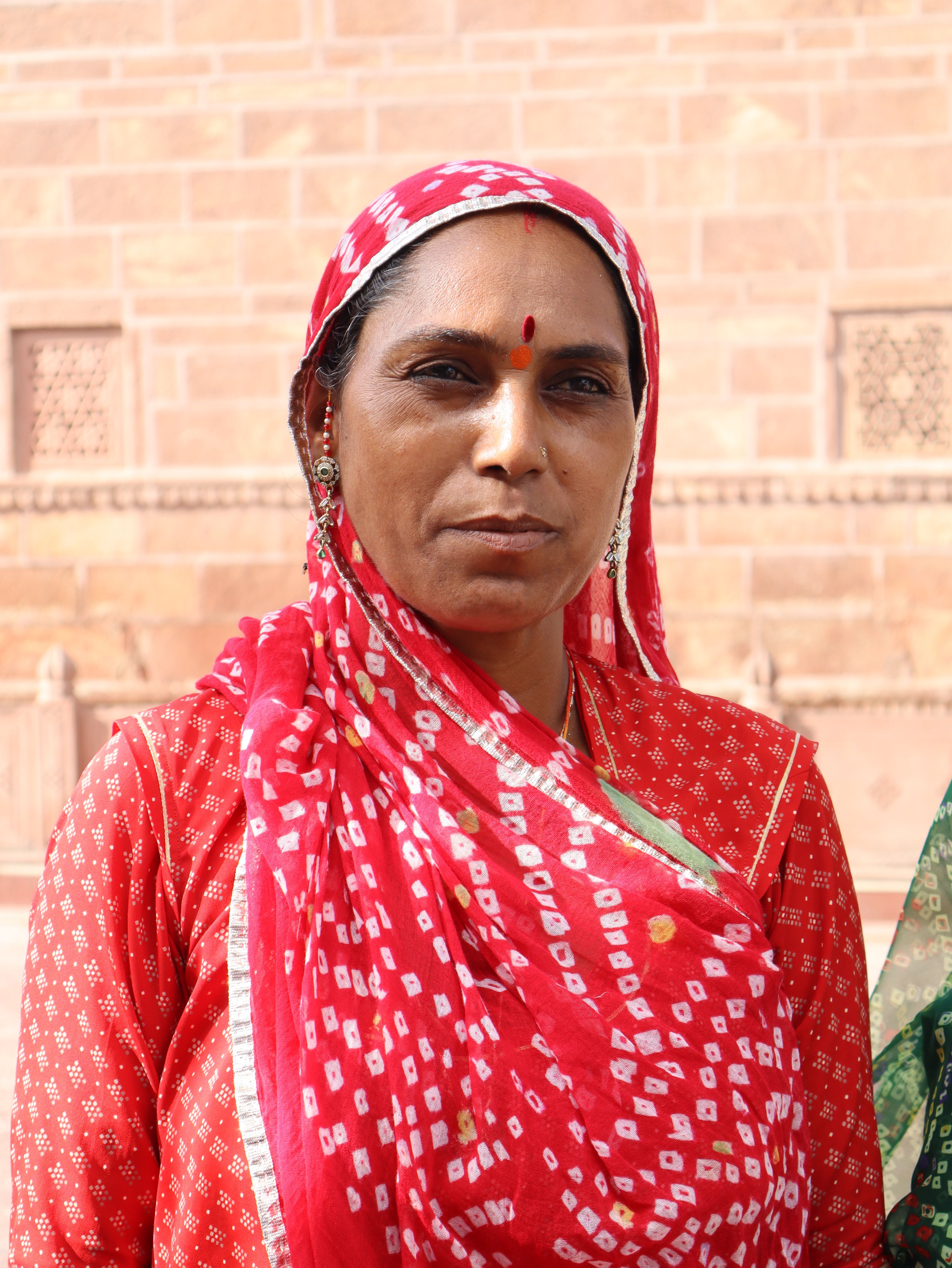 Portrait of a woman in traditional red attire against a textured wall.