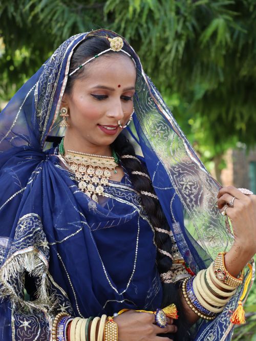 Free Woman in blue traditional attire adorned with jewelry under a tree. Stock Photo