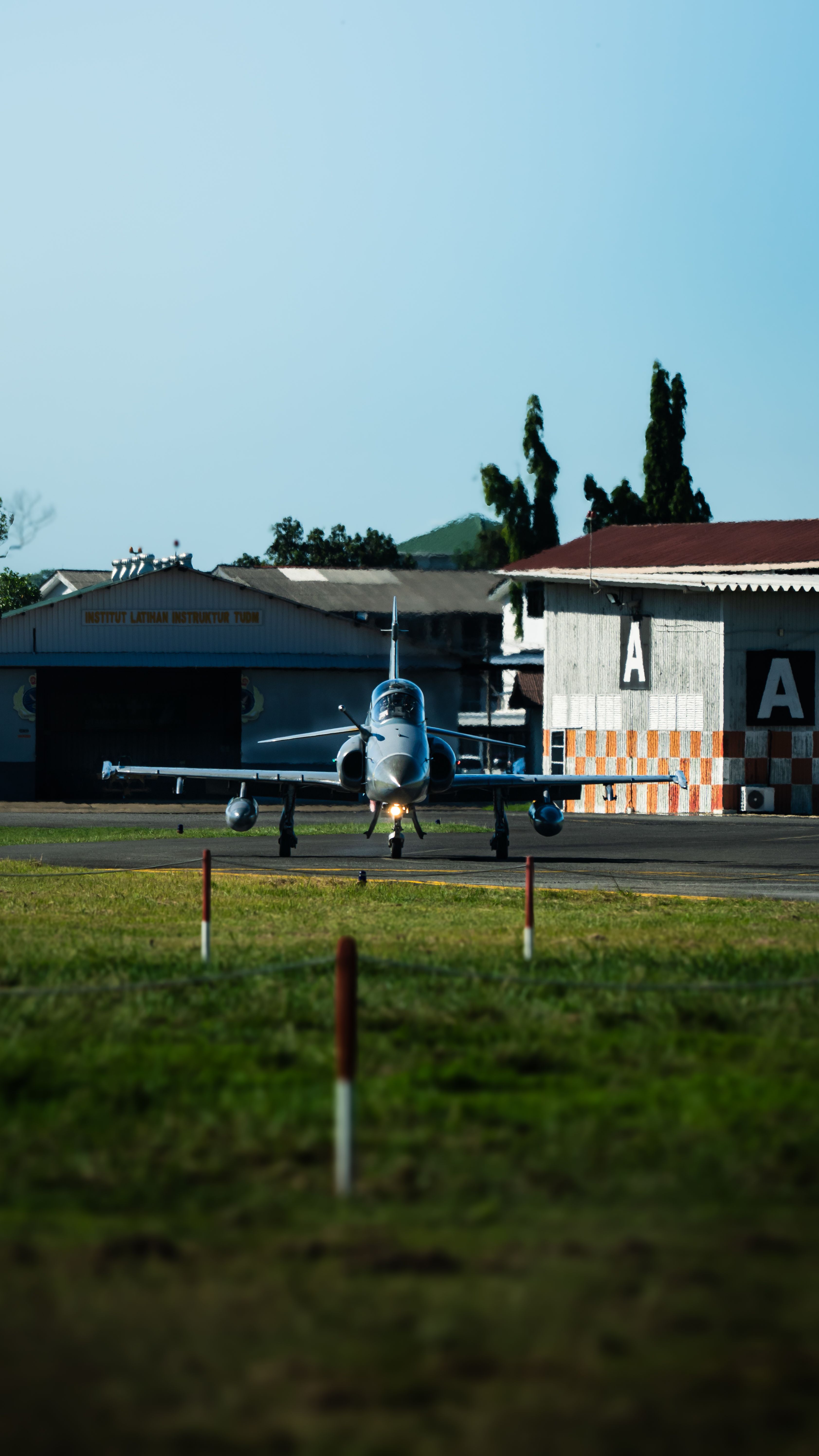 A small jet taxiing on a runway at Alor Setar airport, Malaysia, with clear blue sky.