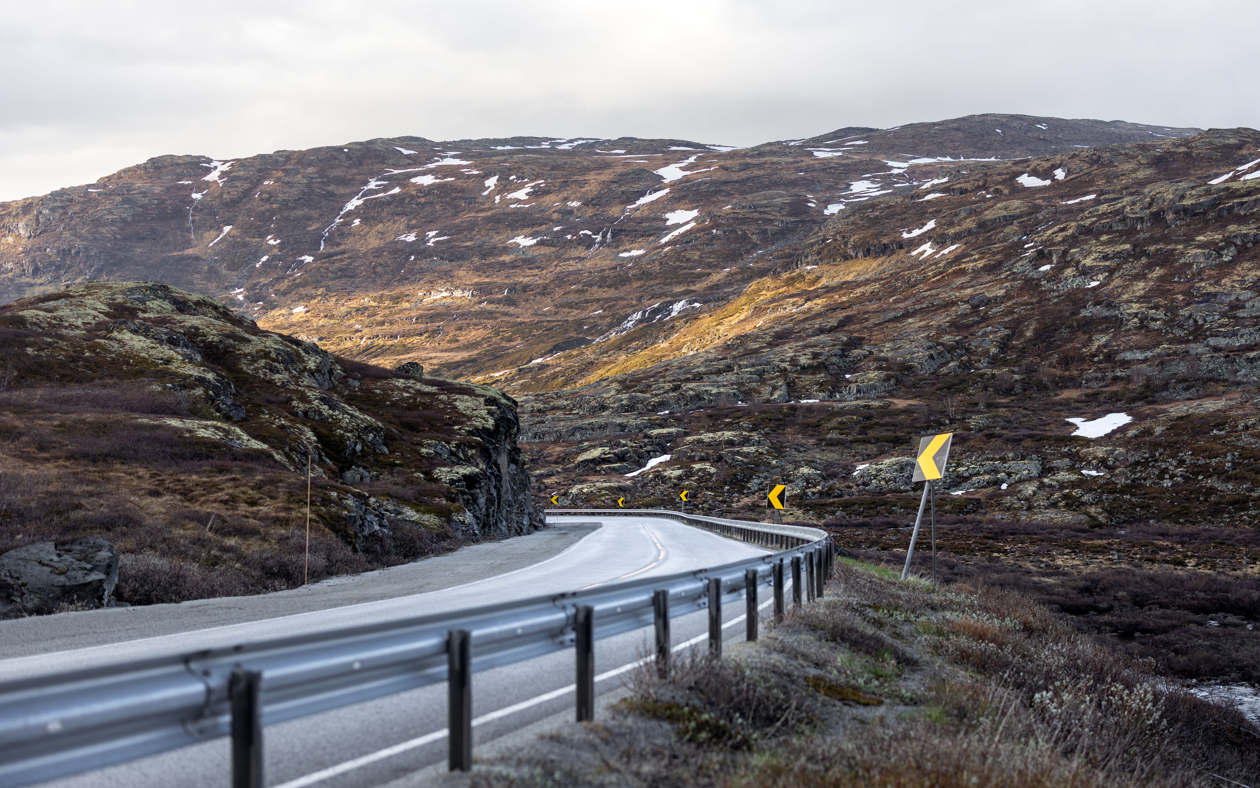 Winding mountain road in Norway with dramatic skies and rugged terrain.