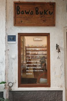 Cozy entrance of an Indonesian bookstore with rustic wooden sign and reflective glass. - Fotografer Sidoarjo