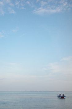A peaceful seascape with a solitary boat floating under a vast sky at dawn.