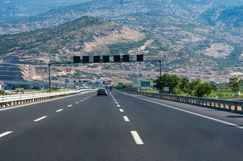Free Long highway with cars traversing through rocky hills under blue skies, perfect travel scene. Stock Photo
