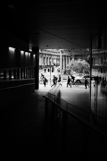Black and white urban street scene in Melbourne with silhouettes of cyclists and pedestrians.