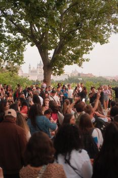 A large diverse crowd gathers under a tree in a scenic park setting.