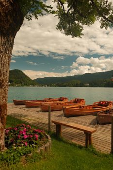 Peaceful lake with wooden boats at dock, lush surroundings and mountain view.