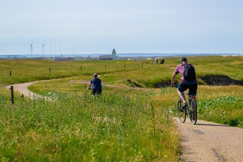 Free Cyclists riding along a coastal path in Lemvig, Denmark, with wind turbines in the background. Stock Photo