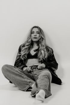 Black and white portrait of a fashionable woman in casual attire sitting on the floor.