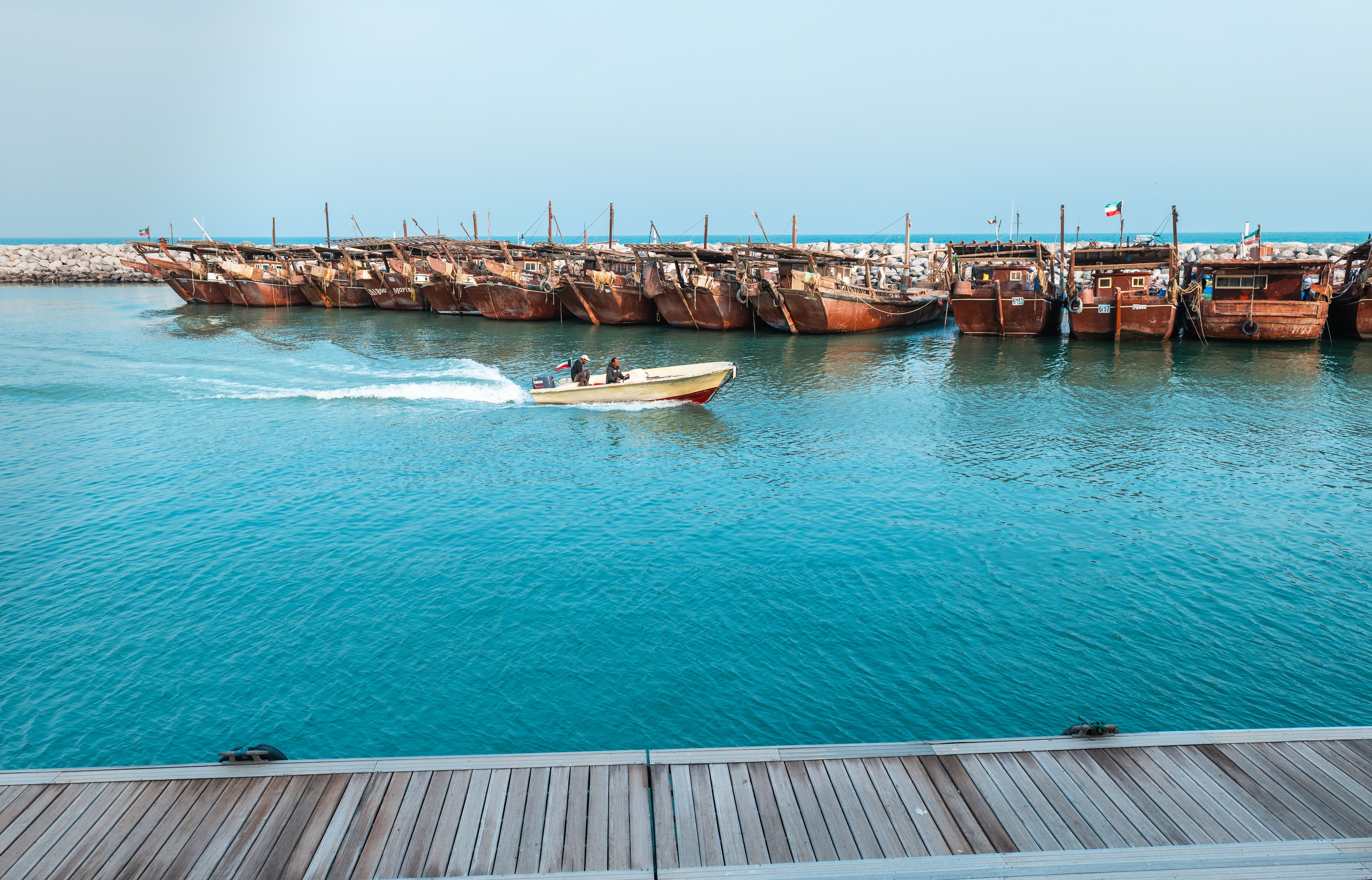 A serene view of traditional wooden dhows docked at a Middle Eastern port with a motorboat passing by.
